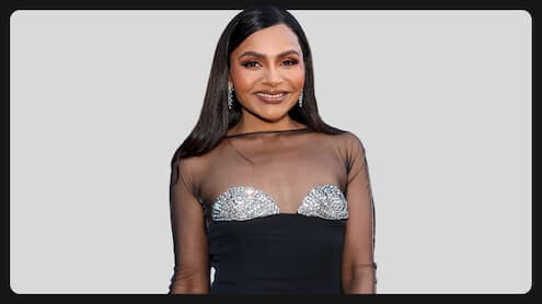Mindy Kaling w czarnej sukni z przezroczystymi rękawami i srebrnymi zdobieniami na jasnym tle